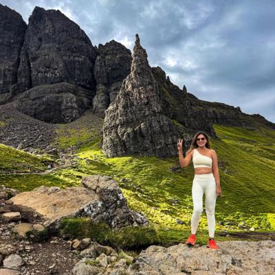 Dipali Trivedi on the green slope below the Old Man of Storr, the basalt pinnacle and Trotternish escarpment towering behind her