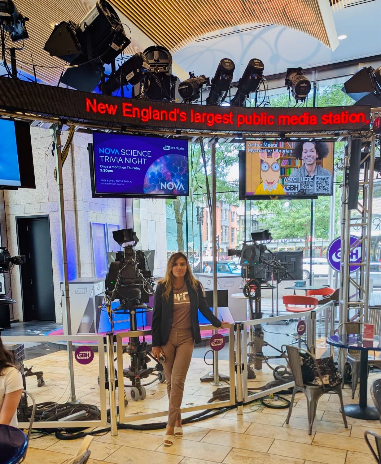 Dipali Trivedi standing on the GBH studio floor in Boston between two television cameras, beneath a marquee reading New England's largest public media station